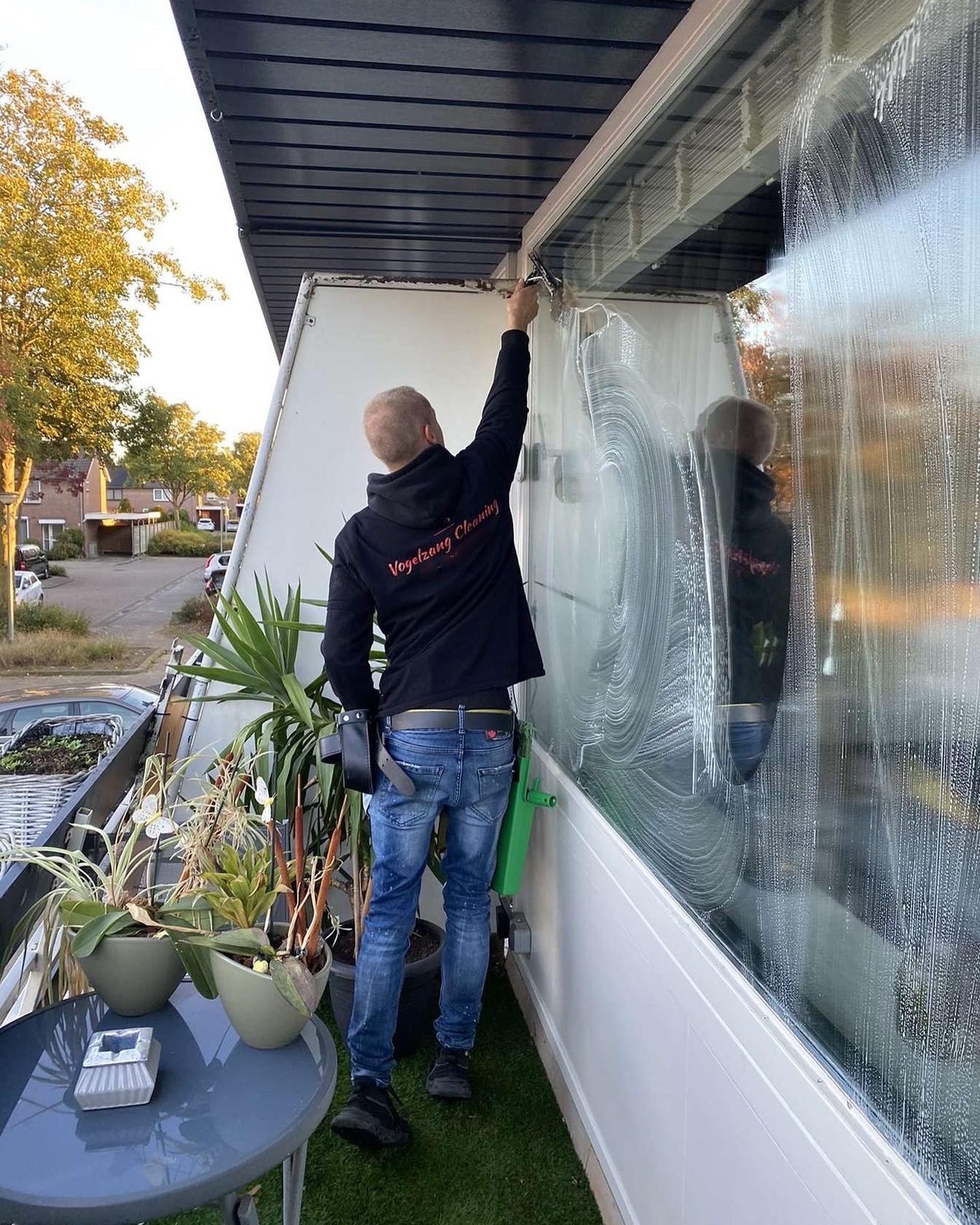 Op een balkon trekt hij de bovenkant van een groot raam droog