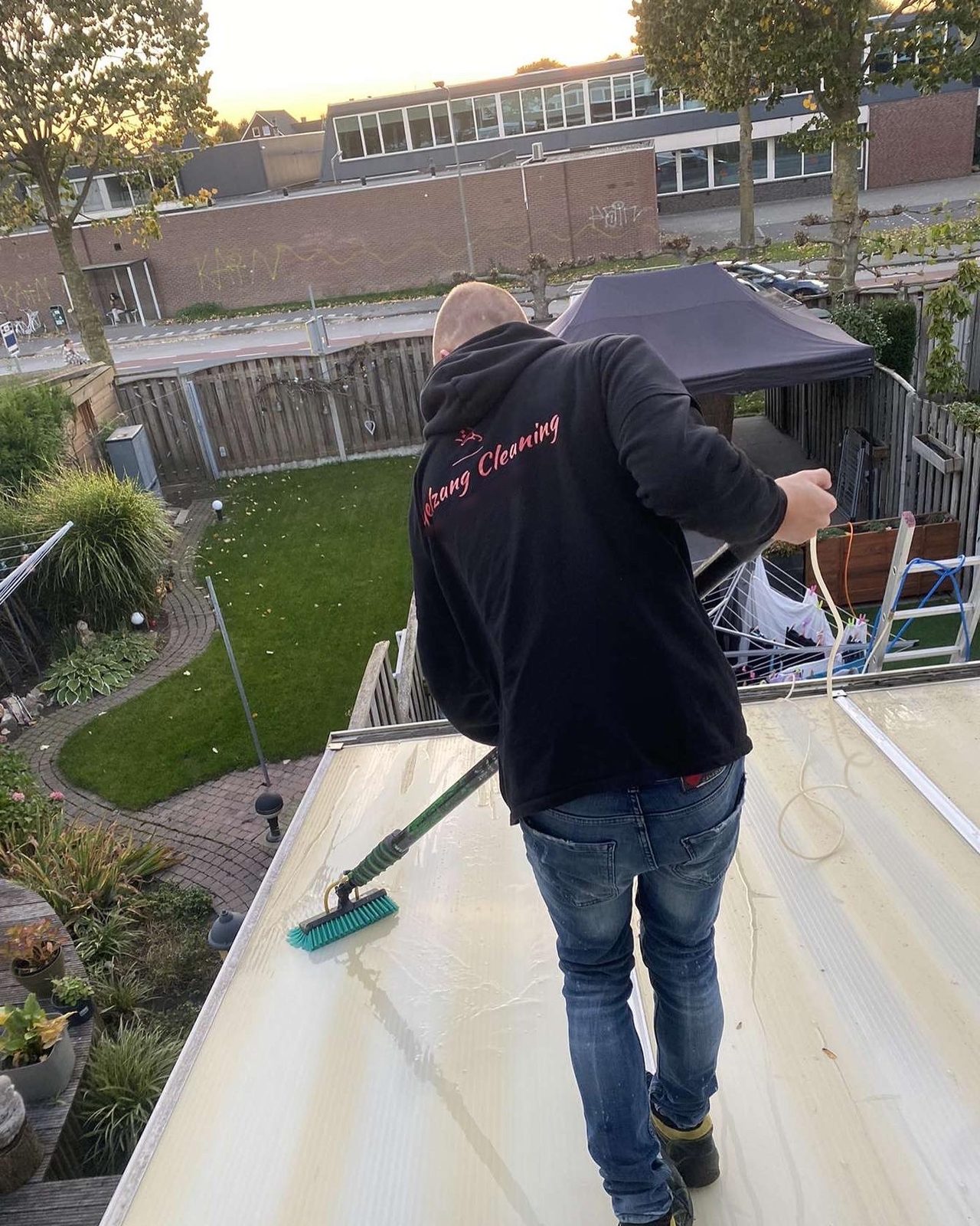 Vogelzang Cleaning op een veranda-dak, met een borstel aan een lange steel