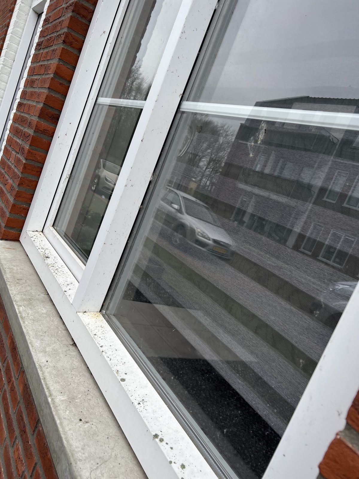 Een wit kozijn met vuil, spetters en groene aanslag op de vensterbank