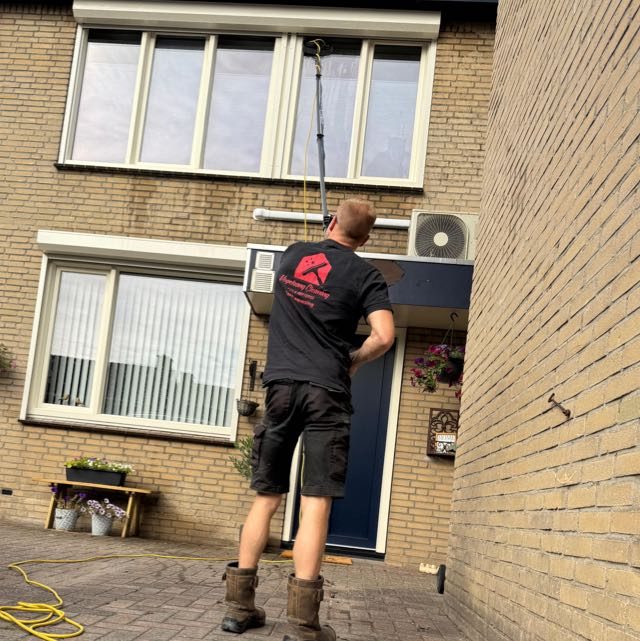 Met een lange telescoopsteel wast hij de ramen op de eerste verdieping, vanaf de grond